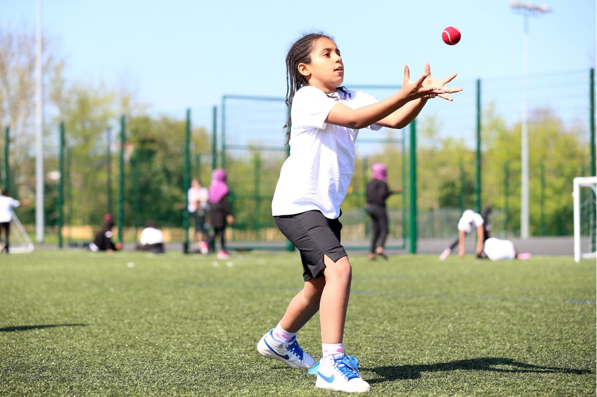 A child catching a ball during an outdoor PE session on the astroturf