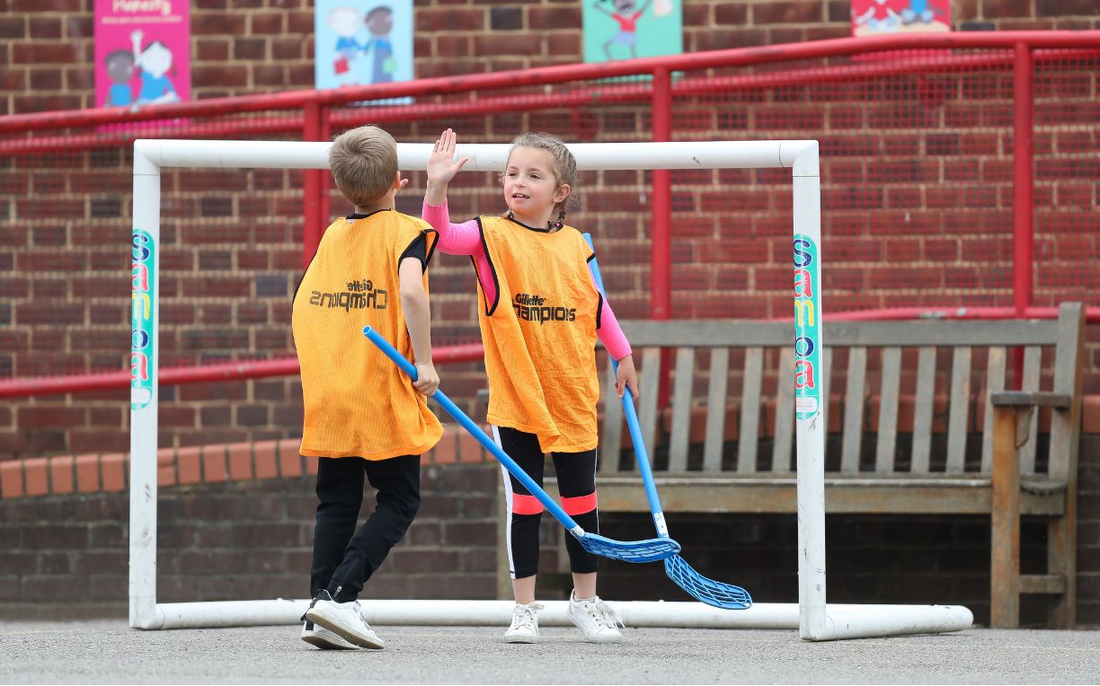 Two children high-fiving in the playground during a Challenge floorball session